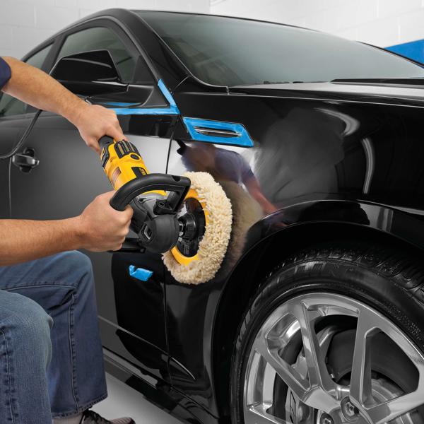 A person using a DEWALT DWP849X polisher to buff the side of a black car, with blue tape applied to certain areas for protection.
